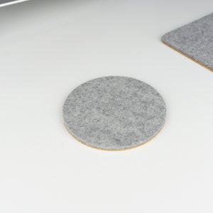A single round felt and cork coaster in light grey felt shown on a white desk surface next to matching light grey wool felt desk mat.