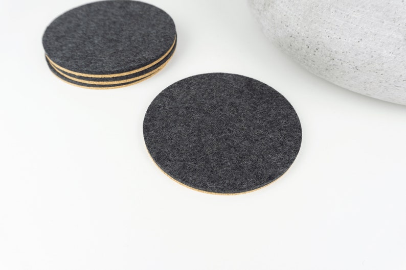 A set of our round black wool felt and cork coasters shown on a white coffee table.