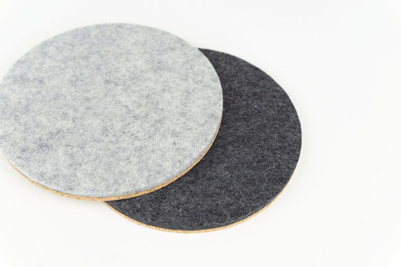 A colour comparison between black and light grey shades of our round wool felt and cork coasters.