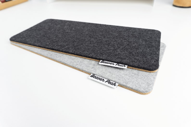 Comparison of black wool felt keyboard mat and grey keyboard mat, both against white desk.