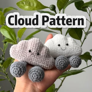 May include: Two crocheted cloud toys, one light pink and one white, each with grey wheels. The pink cloud has a sad face, while the white cloud has a smiling face. The text "Cloud Pattern" is displayed above the clouds.
