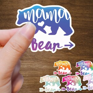 May include: A set of five colorful vinyl stickers featuring a bear silhouette with the text "mama bear" and an arrow. The stickers are in various shades of blue, purple, pink, orange, and yellow.