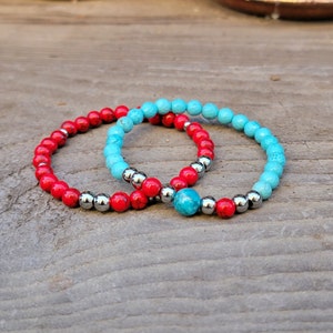 May include: Two beaded bracelets, one red and one blue, with silver accents. The bracelets are stacked on top of each other.