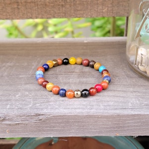 May include: A colorful beaded bracelet with a variety of stones, including red, orange, yellow, blue, green, and brown. The bracelet is made with small, round beads and has a gold accent.