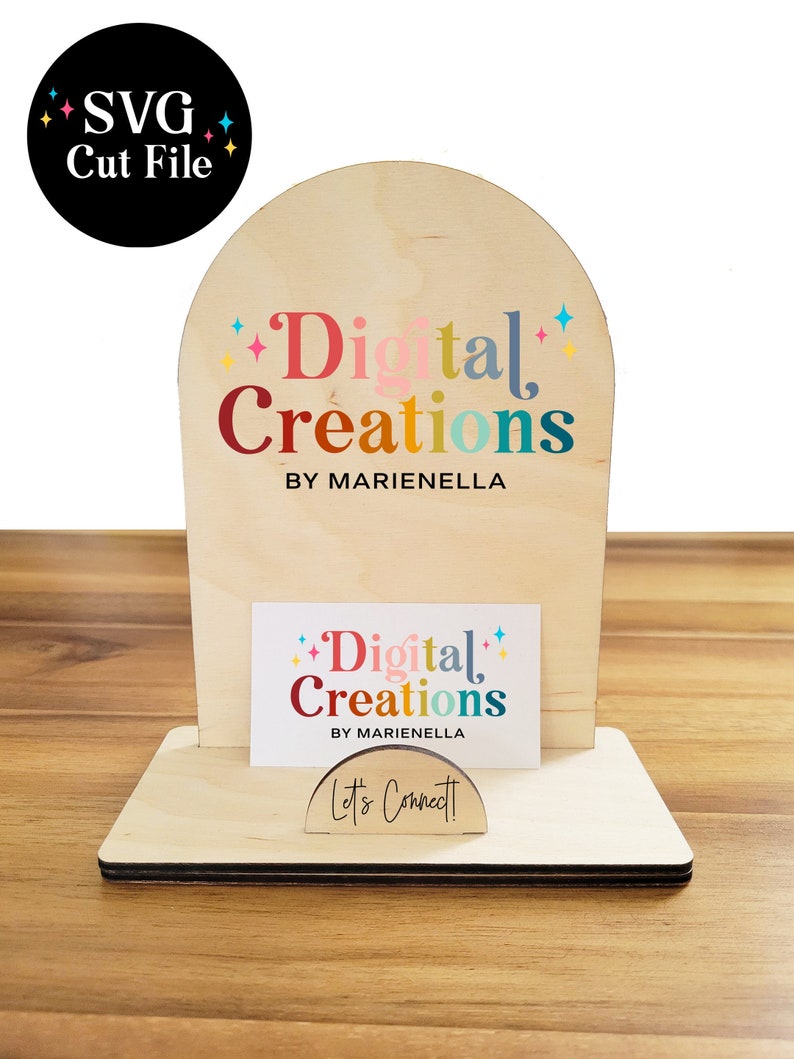 May include: A wooden business card holder with an arched top. The top features the text "Digital Creations by Marianella" in colorful letters. The bottom of the holder has a business card with the same text and a small sign that says "Let's Connect!"