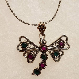May include: A silver dragonfly pendant necklace with green and pink gemstones. The necklace has a delicate chain.