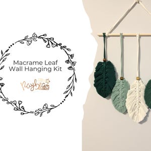 May include: Macrame leaf wall hanging kit with five leaf-shaped macrame pieces in green and white, suspended from a wooden dowel. The kit includes a floral wreath design with the text "Macrame Leaf Wall Hanging Kit".