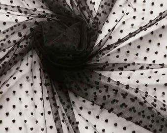 May include: Black tulle fabric with a heart pattern. The fabric is draped and gathered, creating a textured effect. The hearts are evenly spaced across the sheer material, adding a romantic touch. Ideal for crafting or apparel.