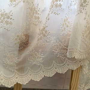 Pu&ograve; includere: Primo piano di un tessuto trasparente bianco sporco con ricami floreali intricati. Il tessuto presenta delicati fiori ricamati e un bordo smerlato. Il design &egrave; dettagliato ed elegante, adatto per l'arredamento della casa o l'artigianato.