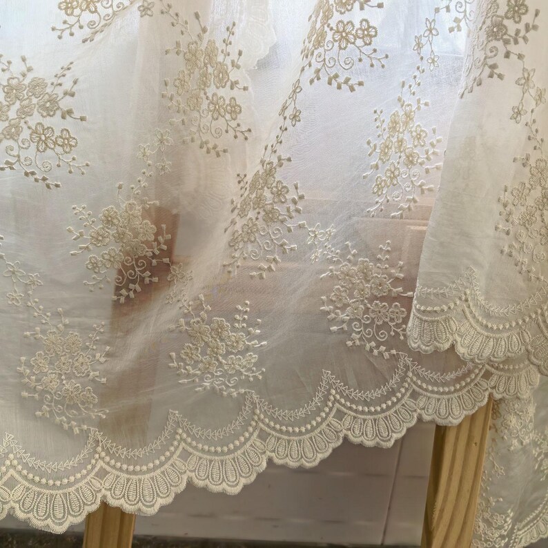 Pu&ograve; includere: Primo piano di un tessuto trasparente bianco sporco con ricami floreali intricati. Il tessuto presenta delicati fiori ricamati e un bordo smerlato. Il design &egrave; dettagliato ed elegante, adatto per l'arredamento della casa o l'artigianato.