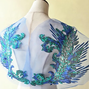 May include: A set of three ceramic mugs with a speckled, cream-colored glaze. Each mug features a different hand-painted floral design in shades of blue, green, and yellow. The mugs have a simple, rounded shape and a comfortable handle.