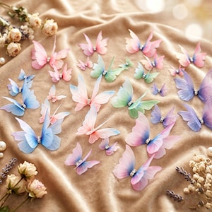 Op de afbeelding: Een verzameling decoratieve vlinderornamenten in verschillende maten, met doorschijnende vleugels in tinten roze, blauw, groen en paars. Elke vlinder heeft een kleine, heldere strass-steen in het midden van het lichaam.