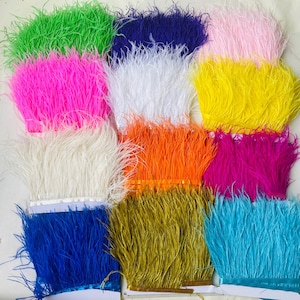 Puede incluir: Una colección de adornos de plumas coloridas en varios tonos, incluyendo verde, rosa, blanco, naranja, amarillo, azul y fucsia. Las plumas están dispuestas en filas, mostrando su textura y colores vibrantes. Ideal para manualidades y adornos.