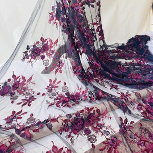 以下が含まれることがあります： 紫とバーガンディの色合いの刺繍の花柄が施された黒いチュール生地。生地は、ビーズのアクセントが付いた詳細な3次元の花のアップリケが特徴で、豪華で質感のある外観を作り出しています。ブライダルウェアや特別な機会の衣服に最適です。