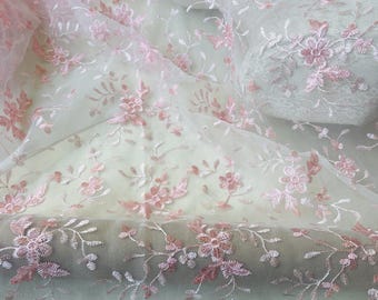 May include: Delicate pink floral embroidered fabric. The sheer material features detailed embroidery of flowers and leaves in varying shades of pink. The fabric has a scalloped edge, adding a decorative touch. Ideal for crafting or apparel.
