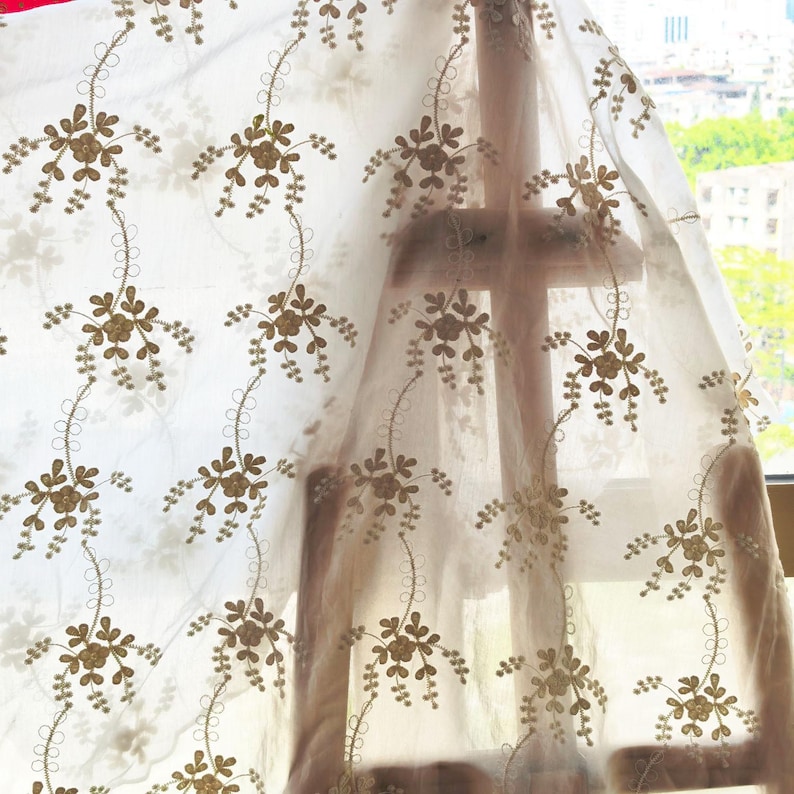 May include: Sheer white curtain with an embroidered floral pattern in shades of gold and brown. The delicate design features stylized flowers and vines, creating a soft, elegant look. The curtain is semi-transparent, allowing light to filter through.