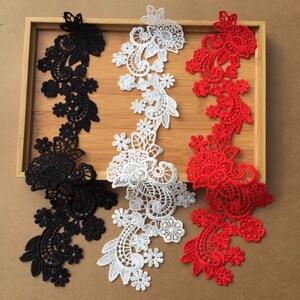 May include: Three decorative lace appliques in black, white, and red, arranged on a wooden tray. Each applique features a floral and scroll design, ideal for embellishing garments or crafts. The intricate details and contrasting colors make them visually appealing.