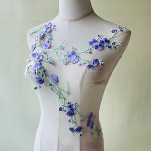 Peut inclure: Applique florale avec des fleurs violettes brodées et des tiges vertes. Le motif est présenté sur un mannequin, mettant en valeur les détails délicats du tissu et des coutures. Cette applique décorative convient à divers projets d'artisanat.