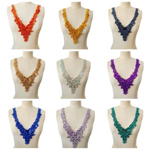 Può includere: Nove applicazioni per scollatura con perline in vari colori, tra cui rosso, oro, blu navy, bronzo, argento, viola, blu, lavanda e verde acqua. Ogni applicazione ha un design a forma di V, esposto su un manichino.