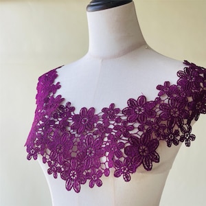 Puede incluir: Un cuello de encaje floral morado oscuro exhibido en un maniquí. El encaje está intrincadamente diseñado con múltiples patrones de flores. El cuello es de un tono morado vibrante, y los detalles delicados son claramente visibles.