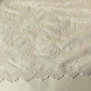 Pu&ograve; includere: Tessuto in pizzo color avorio con ricami floreali. Il tessuto presenta un bordo smerlato con un motivo delicato e ripetuto. Il ricamo &egrave; dettagliato e aggiunge consistenza al materiale morbido e trasparente. Ideale per abiti da sposa, abiti o progetti decorativi.
