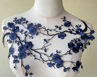 Op de afbeelding: Marineblau bloemen kanten applicatie met geborduurde bloemen en takken. De applicatie is ontworpen om op stof te worden genaaid en wordt op een mannequin getoond.