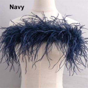 Op de afbeelding: Marineblauwe verenboa, getoond op een mannequin. De boa is gemaakt van lange, zachte veren. Het woord "Navy" staat linksboven afgedrukt. Decoratief accessoire.