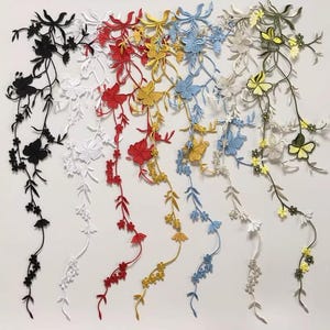 May include: A collection of embroidered floral appliques in various colors, including black, white, red, yellow, and blue. Each applique features detailed flower and leaf designs, perfect for embellishing clothing or crafts.