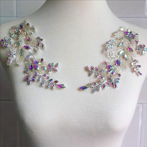 Peut inclure: Deux appliques florales ornées, composées de strass irisés et de perles argentées. Elles sont présentées sur un mannequin blanc, mettant en valeur leur design et leur potentiel d'utilisation sur des vêtements ou accessoires.