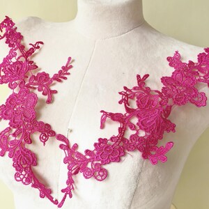 May include: Two pieces of fuchsia lace trim, featuring floral and leaf patterns. The lace is displayed on a white dress form, showcasing the intricate details and openwork design. Ideal for embellishing garments or craft projects.