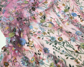 May include: Close-up of a sheer, pink fabric with intricate floral embroidery. The embroidery features a variety of colorful flowers in shades of blue, pink, yellow, and green, with delicate green stems and leaves. The fabric is likely used for apparel or decorative purposes.
