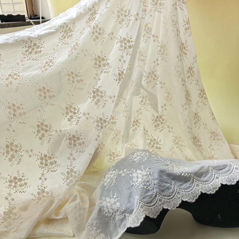 Pu&ograve; includere: Tessuto bianco sporco con un delicato motivo floreale in una tonalit&agrave; pi&ugrave; chiara. Il tessuto &egrave; drappeggiato, mostrando la sua consistenza e gli intricati dettagli dei fiori ricamati. &Egrave; visibile anche un pezzo di tessuto separato con un bordo smerlato.