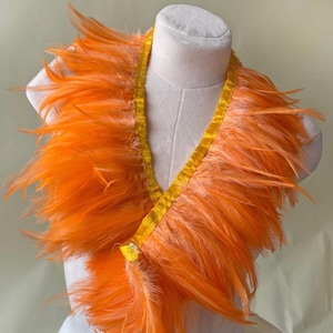 Peut inclure: Un boa en plumes orange avec un col en ruban de satin jaune. Le boa est présenté sur un buste de mannequin blanc. Les plumes sont d'un orange vif et le ruban est d'un jaune vif.