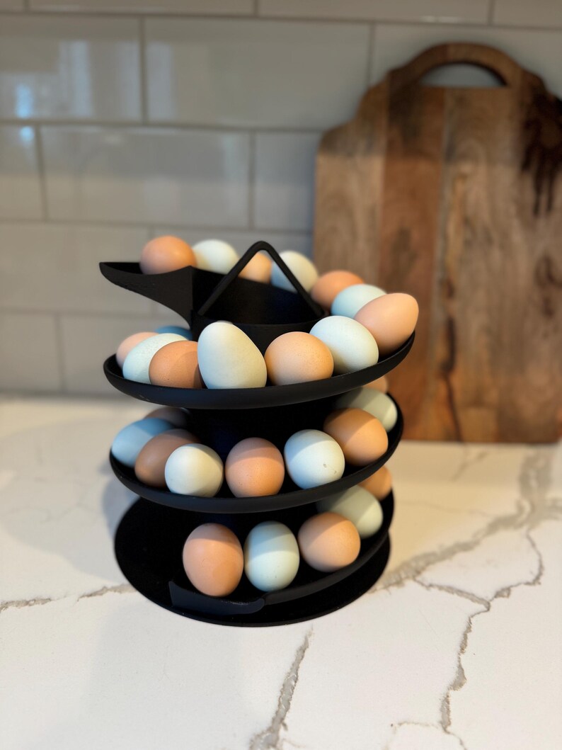 Puede incluir: Un soporte negro para huevos de tres niveles lleno de una variedad de huevos en tonos marrones, azules y blancos. El soporte es de metal y tiene un dise&ntilde;o circular. Los huevos est&aacute;n dispuestos en espiral.