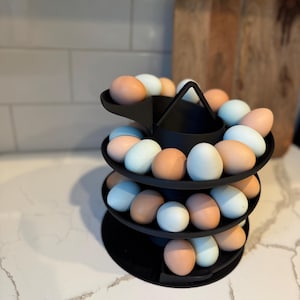 Puede incluir: Un soporte negro para huevos de tres niveles lleno de huevos marrones y azules. El soporte tiene un asa en la parte superior y est&aacute; dise&ntilde;ado para exhibir los huevos en forma de espiral. Los huevos son de diferentes tonos.