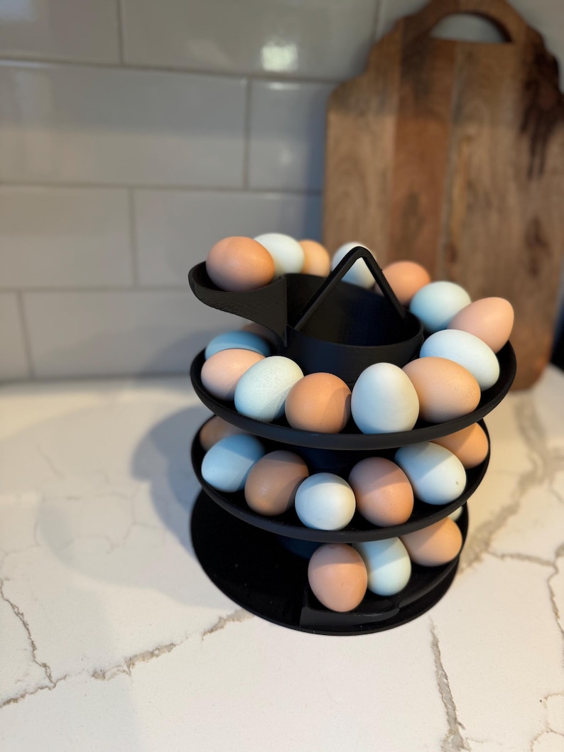 Puede incluir: Un soporte negro para huevos de tres niveles lleno de huevos marrones y azules. El soporte tiene un asa en la parte superior y est&aacute; dise&ntilde;ado para exhibir los huevos en forma de espiral. Los huevos son de diferentes tonos.