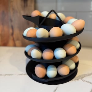 Puede incluir: Un soporte negro para huevos de tres niveles lleno de huevos marrones, azules y blancos. El soporte de metal para huevos tiene un dise&ntilde;o moderno. Ideal para el almacenamiento en la cocina, contiene una variedad de huevos.