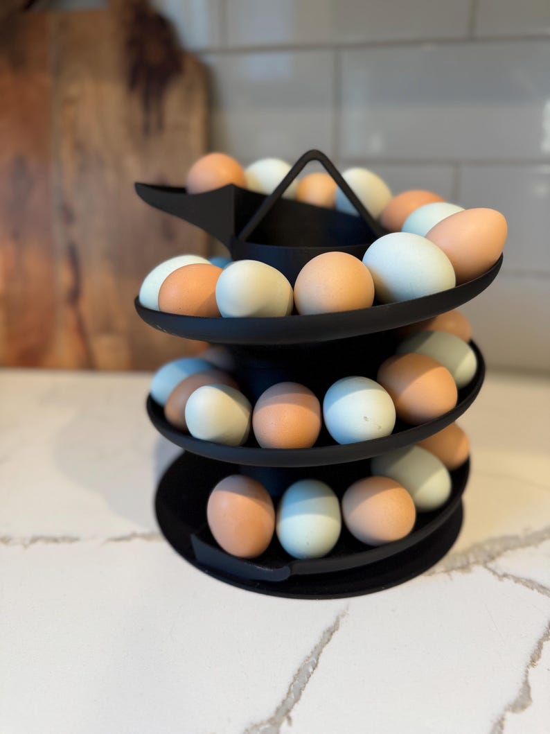 Puede incluir: Un soporte negro para huevos de tres niveles lleno de huevos marrones, azules y blancos. El soporte de metal para huevos tiene un dise&ntilde;o moderno. Ideal para el almacenamiento en la cocina, contiene una variedad de huevos.