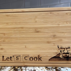 May include: A brown wooden cutting board with the text "Let's Cook" and a chemical symbol for sulfur and carbon. The board also has a burned-in image of a man with a mustache and glasses.