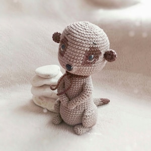 May include: A crocheted brown meerkat toy with black eyes and a brown nose. The toy is sitting on a stack of white stones.