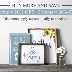 May include: Three wooden signs with inspirational messages. The signs are on a wooden surface. The signs read "Be the reason someone smiles today", "Be Happy", and "Gather".