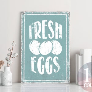 Könnte beinhalten: Ein blaues und weißes Schild mit dem Text "FRESH EGGS" in weißen Buchstaben. Das Schild hat einen abgenutzten Look und drei weiße Eier sind in der Mitte abgebildet.