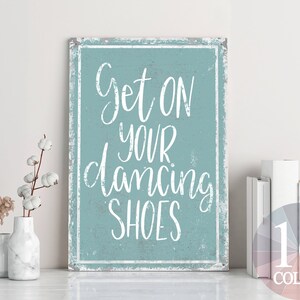 以下が含まれることがあります： 白い文字で「Get on your dancing shoes」と書かれた薄い青色の看板。看板は、使い古されたビンテージな外観をしています。
