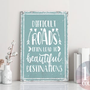 Puede incluir: Un letrero azul y blanco con el texto "Difficult Roads Often Lead To Beautiful Destinations". El letrero tiene un aspecto desgastado y está enmarcado con un borde de madera.