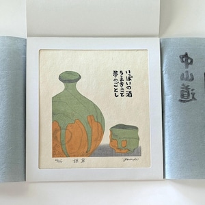 May include: An artistic print featuring a green and orange sake bottle and cup. Japanese text is visible on the print. The print is presented in a white frame, with blue paper on either side.