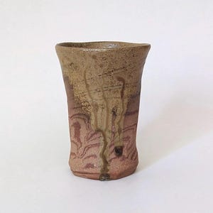 Könnte beinhalten: Eine handgefertigte Keramikvase mit einer einzigartigen, strukturierten Oberfläche. Die Vase zeigt eine Mischung aus Braun- und Rotbrauntönen mit vertikalen Streifen und einer leicht unregelmäßigen Form. Das Design ist organisch und erdig, für die Inneneinrichtung.