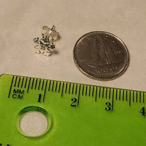 Op de afbeelding: Een zilveren sneeuwvlok oorbel met een heldere strass in het midden. De oorbel is ongeveer 1,25 cm in diameter en wordt getoond naast een Canadese dime ter vergelijking van de grootte.