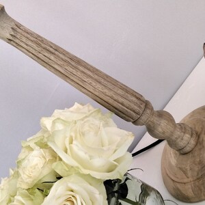 Puede incluir: Un candelabro de madera con un dise&ntilde;o tallado, una escultura de conejo de bronce y un ramo de rosas blancas. El candelabro tiene una base redonda y un tallo largo y texturizado. El conejo est&aacute; en posici&oacute;n de salto.