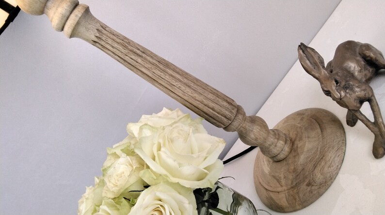 Puede incluir: Un candelabro de madera con un dise&ntilde;o tallado, una escultura de conejo de bronce y un ramo de rosas blancas. El candelabro tiene una base redonda y un tallo largo y texturizado. El conejo est&aacute; en posici&oacute;n de salto.