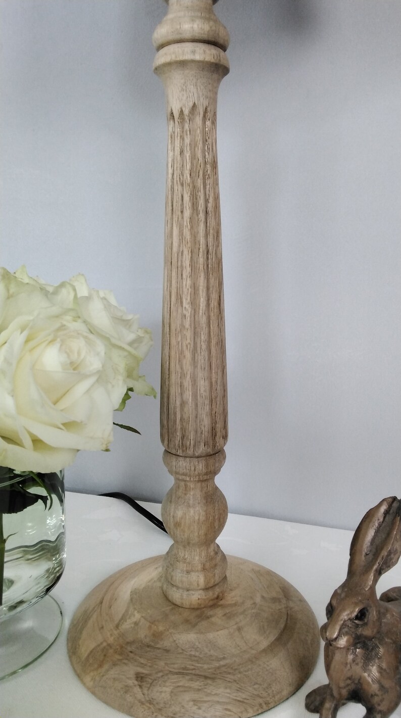 Puede incluir: L&aacute;mpara de madera con acabado marr&oacute;n claro. La l&aacute;mpara tiene una base redonda y una columna estriada. Tambi&eacute;n se ve una figura de conejo de bronce y un jarr&oacute;n con rosas blancas.